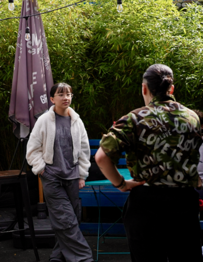 A photo of four young people and one adult. The adult has their back to the camera and the young people are facing the camera and listening intently to the adult.