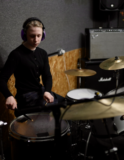 A young person wearing headphones and playing the drums.