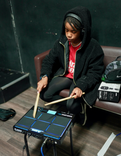 A young person holding two drumsticks above a drum pad, as if they are playing the drum pad.