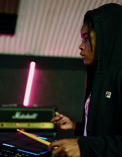 A young person holding a drumstick in front of a drum pad.